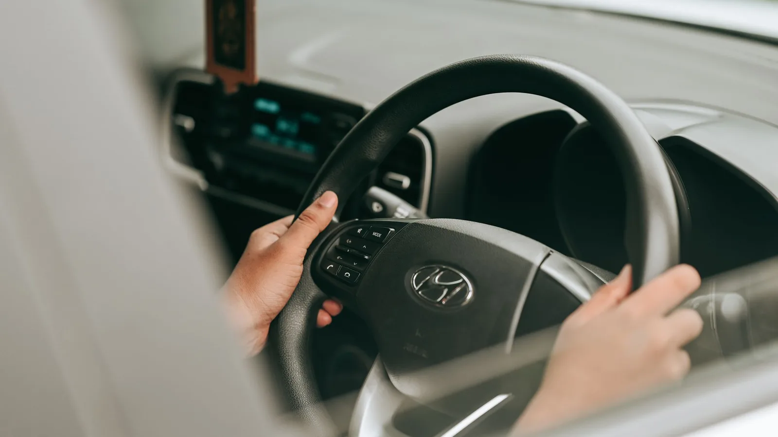 Hands on the steering wheel of a right-hand-drive car with the dashboard controls in view